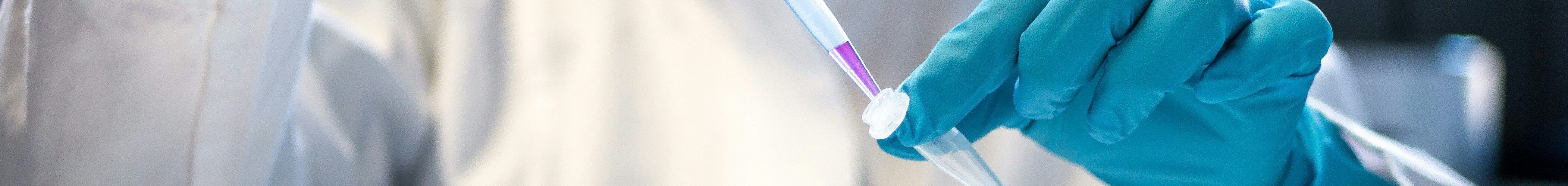 A photo of a woman with nitrtile gloves on pipetting a purple solution into an eppendorf