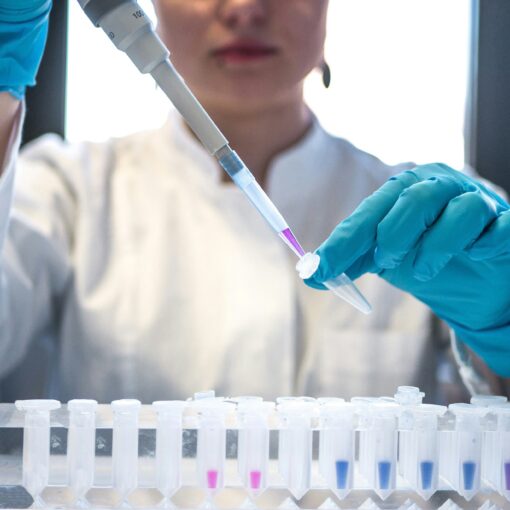 A photo of a woman with nitrtile gloves on pipetting a purple solution into an eppendorf